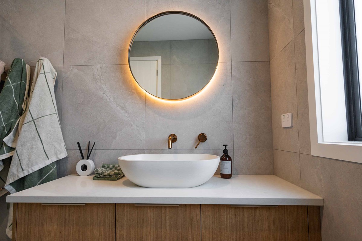 Laura and Shaun's ensuite which features a wooden vanity and basin on top with an LED backlit circular mirror. Simple and aesthetic, this is one of Laura's favourite places in the home as it features a double headed shower.