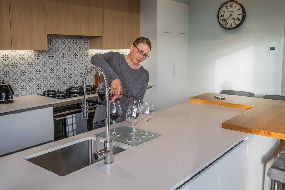 Suzanne, in her kitchen, with one of her highlights of the home, the kitchen splashback. Pouring us a glass of Pinot straight from the in floor wine cellar, as they share what they love about their new home and their experience with David Reid Homes.