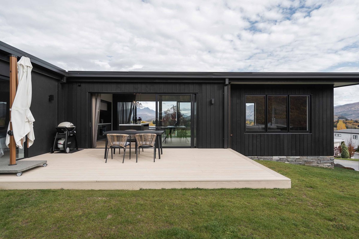 The outdoor living area features a light coloured patio to match the light timber flooring in the kitchen and dining area. This is a big contrast to the dark vertical weatherboard cladding.